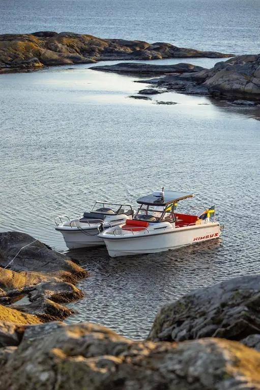 Two boats moored in a calm bay, surrounded by rocky shores and shimmering water, one marked "NIMBUS.